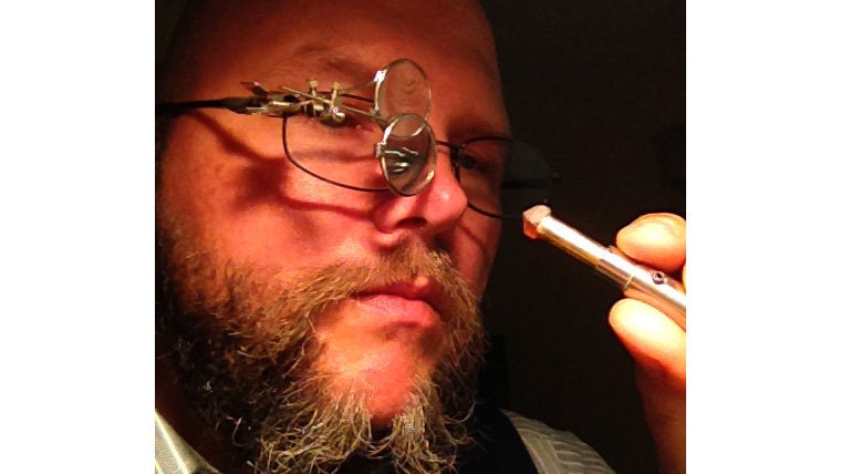 Kelly examining a gemstone with a magnifying loupe in his lapidary studio
