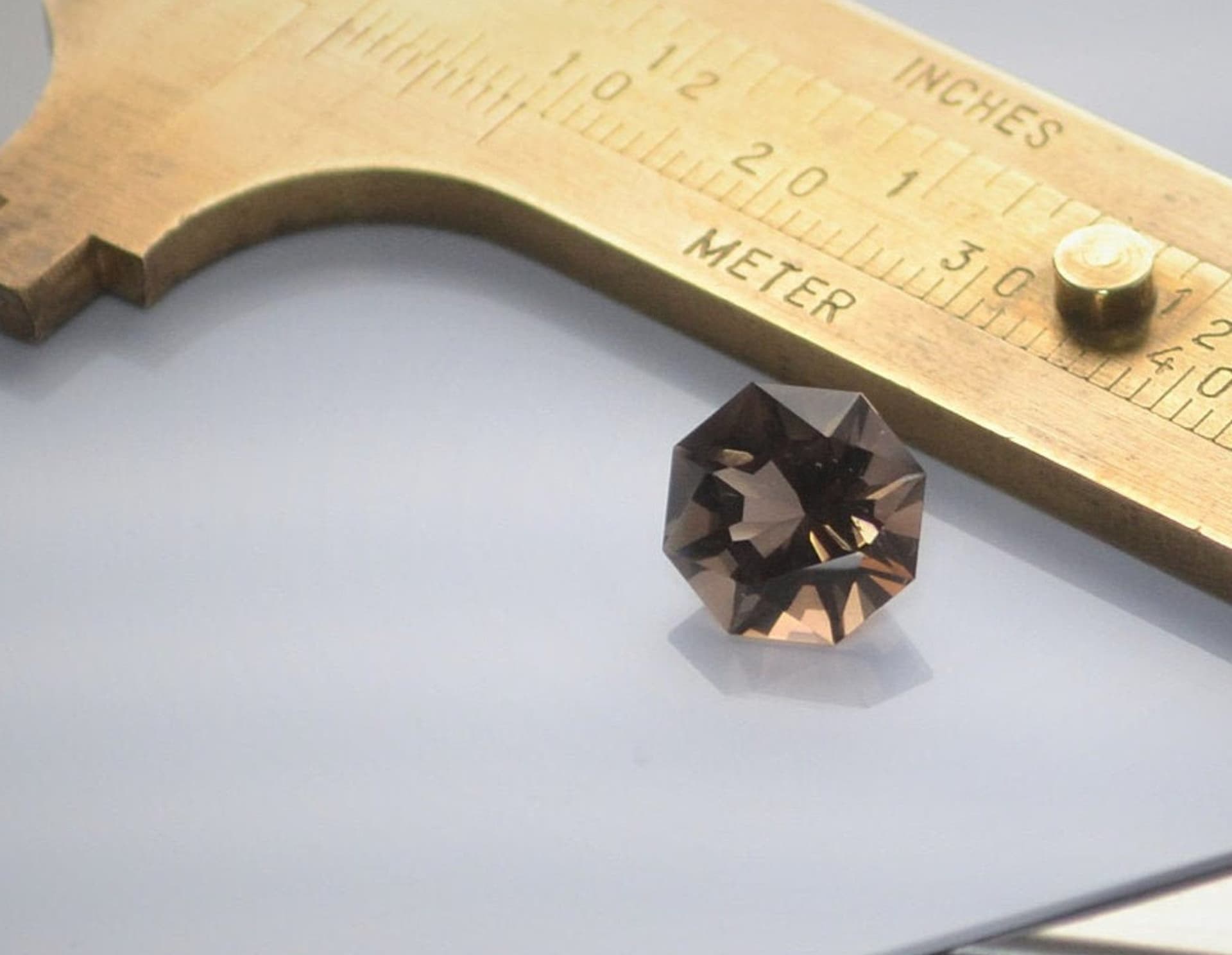 Custom octagon-cut smoky quartz beside a measuring gauge